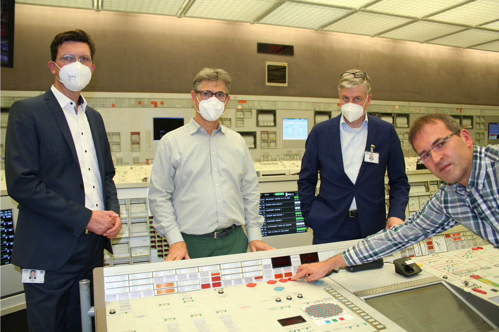 Eine Gruppe von vier Personen in einem industriellen Kontrollraum, die ein Bedienfeld betrachten.