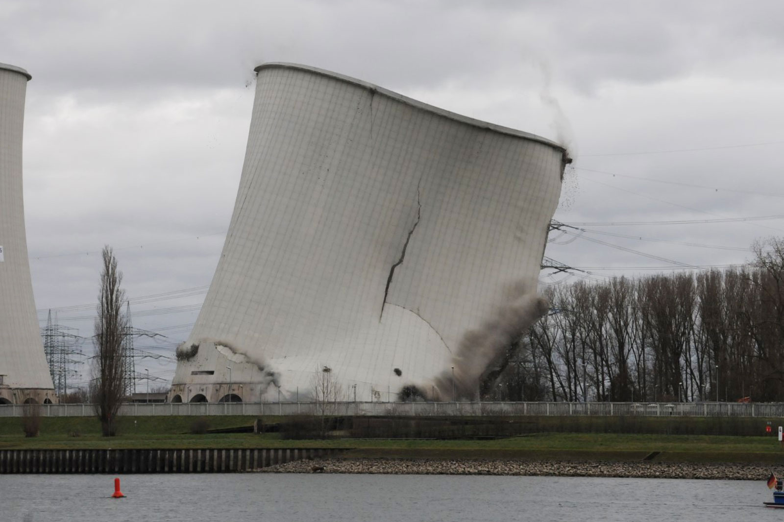 Zwei Kühltürme eines Kraftwerks stürzen ein und erzeugen Rauch und Trümmer gegen einen bewölkten Himmel.