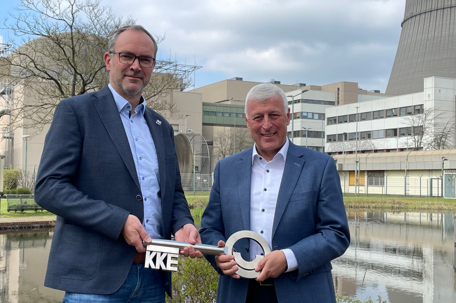 Zwei Männer halten einen großen Metallschlüssel, der eine Partnerschaft symbolisiert, vor einem industriellen Hintergrund.