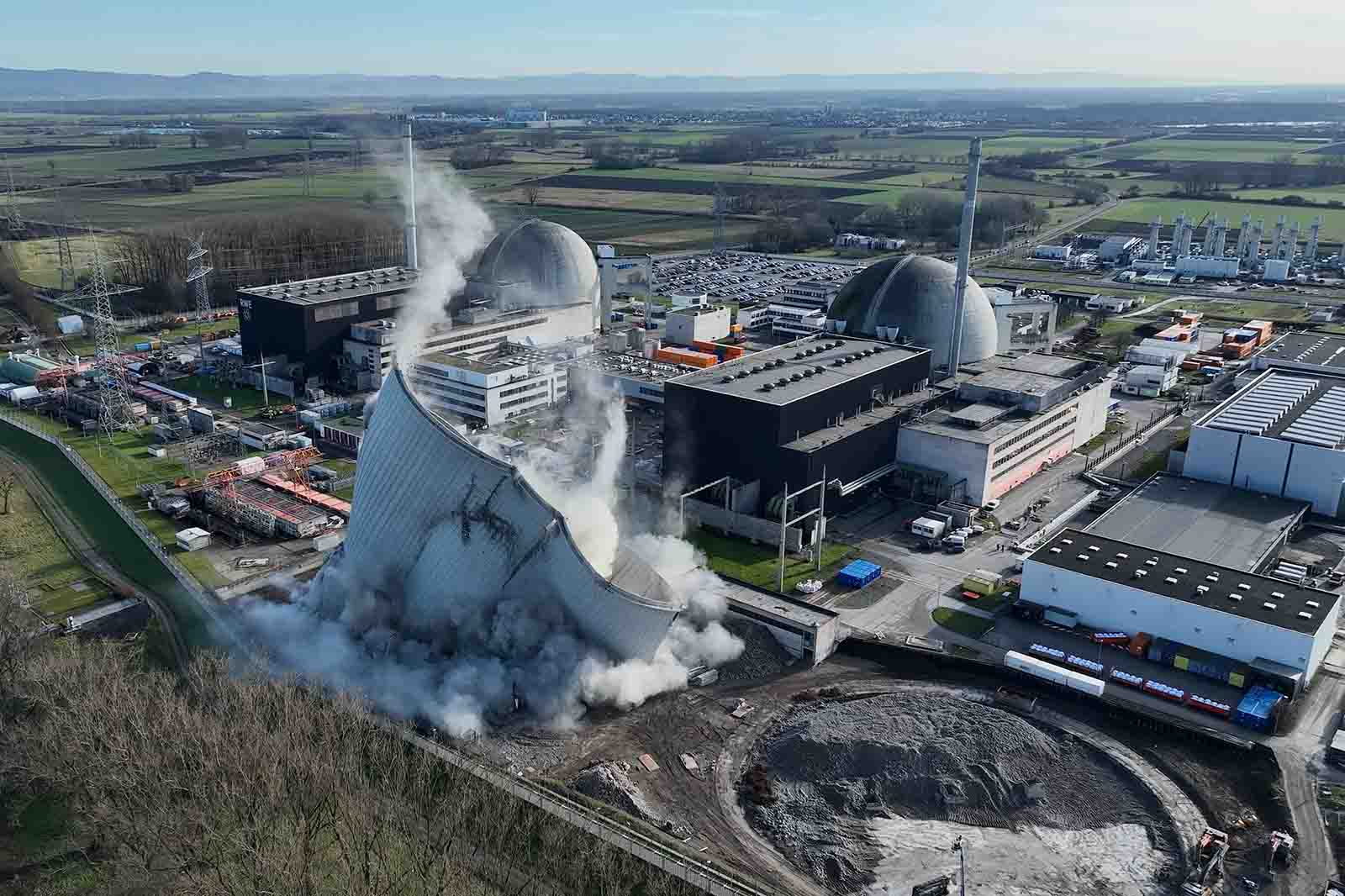 Luftaufnahme eines Kühlturms, der abgerissen wird, mit aufsteigendem Rauch und Staub von der einstürzenden Struktur.