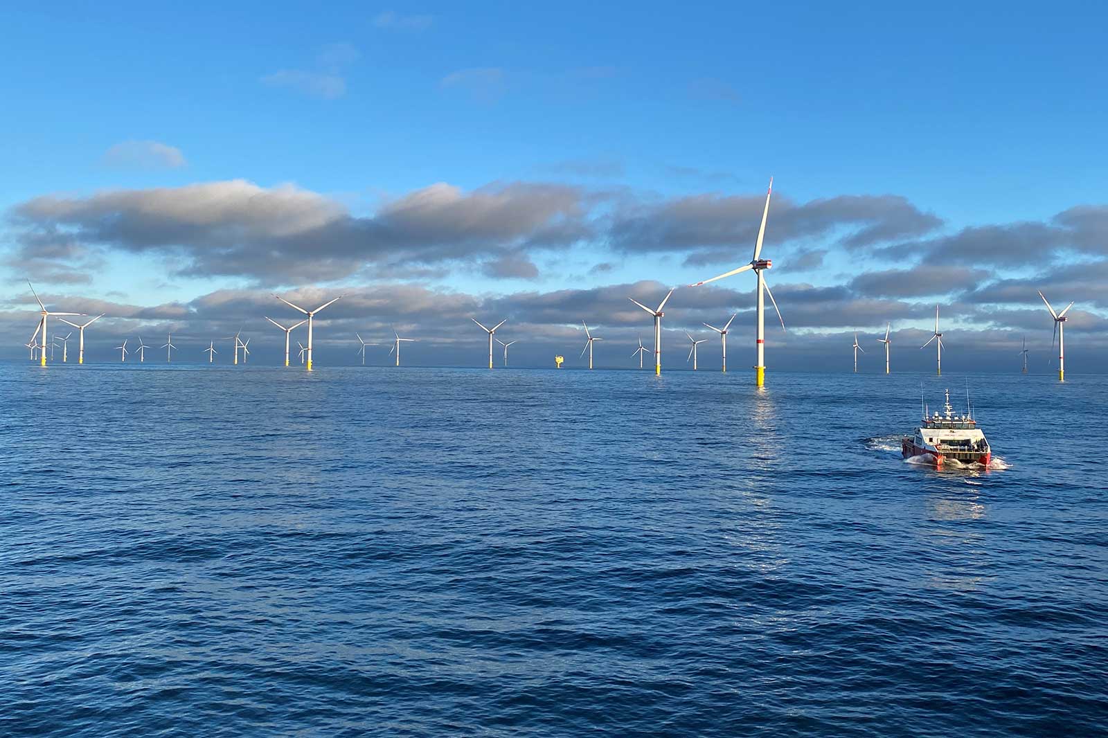 Ein Offshore-Windpark mit mehreren Windturbinen und einem Boot, das über das ruhige Wasser fährt.