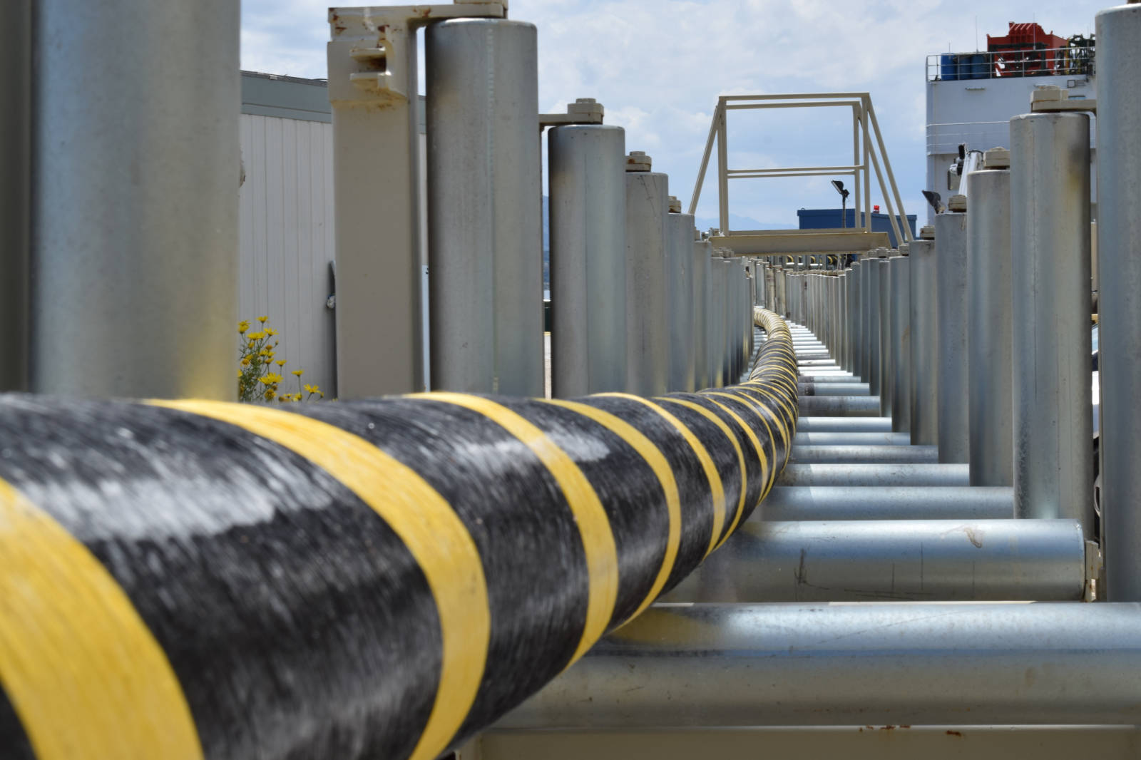 A view of a long, black and yellow striped hose on metallic supports, with a cloudy sky in the background.