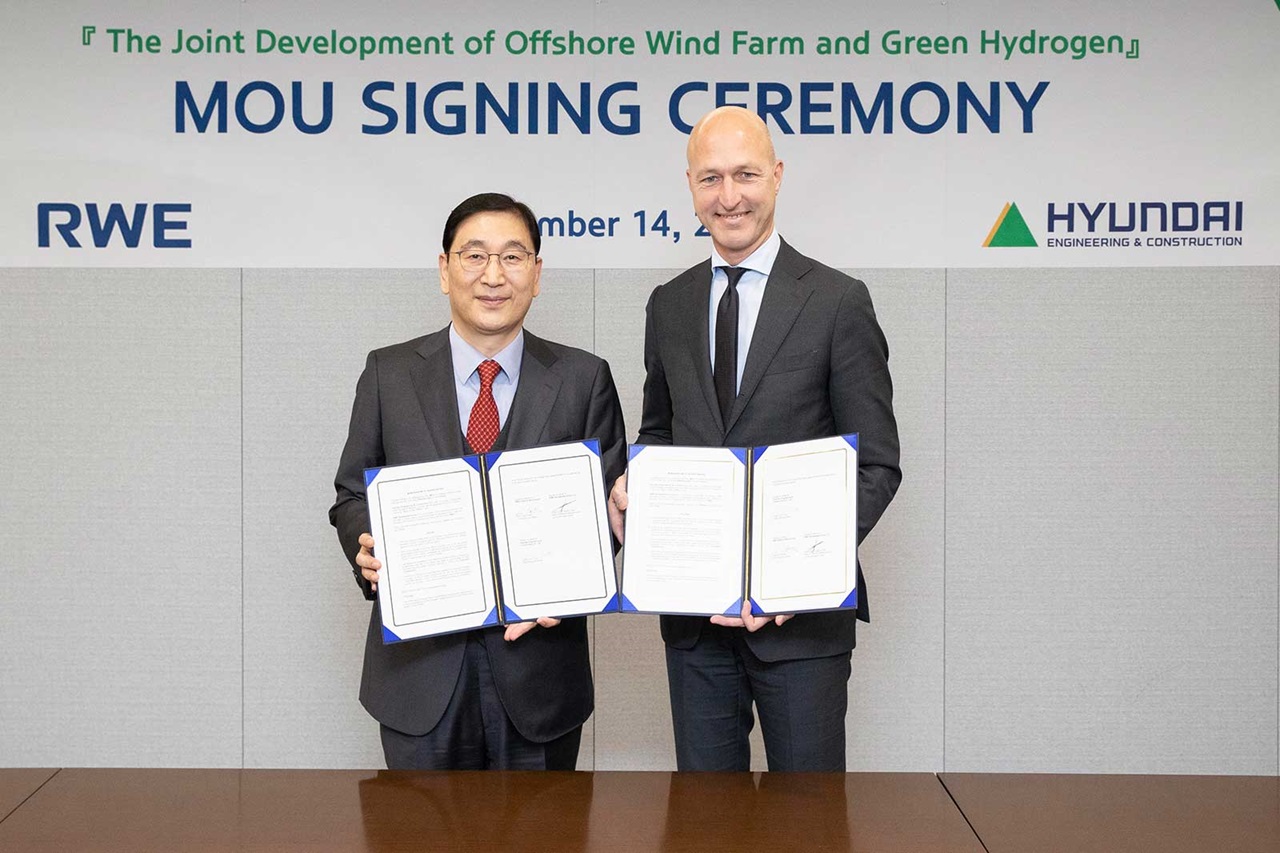 Two individuals stand at a table holding signed documents, with a backdrop for an MOU signing ceremony related to offshore wind farms.