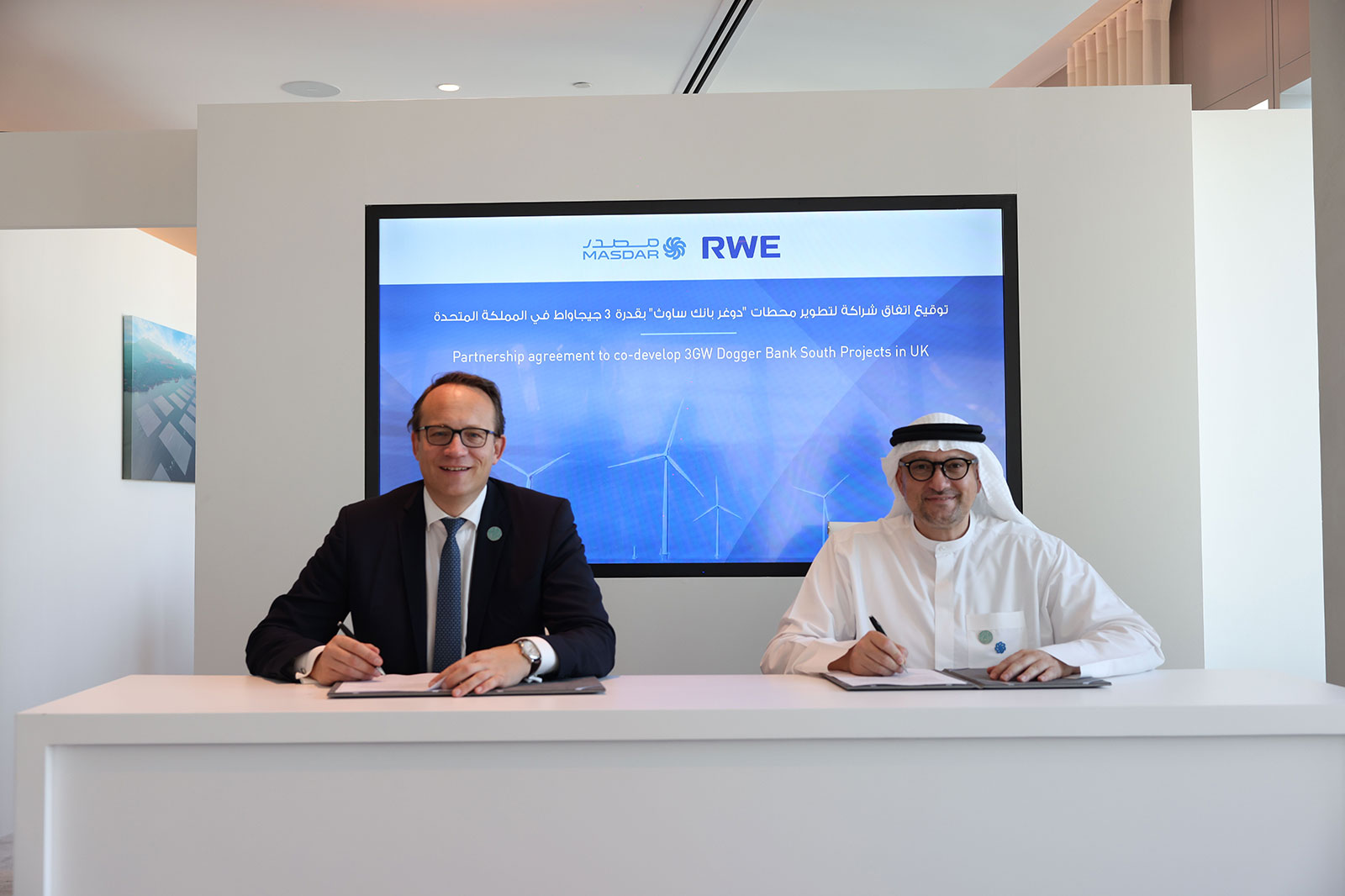 Two individuals are signing an agreement for collaboration on UK projects, in front of a screen displaying the Masdar and RWE logos.