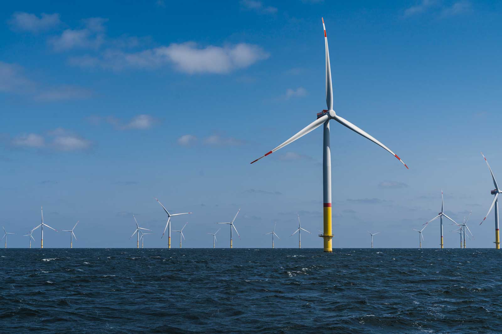 A group of wind turbines in the sea under a clear blue sky.