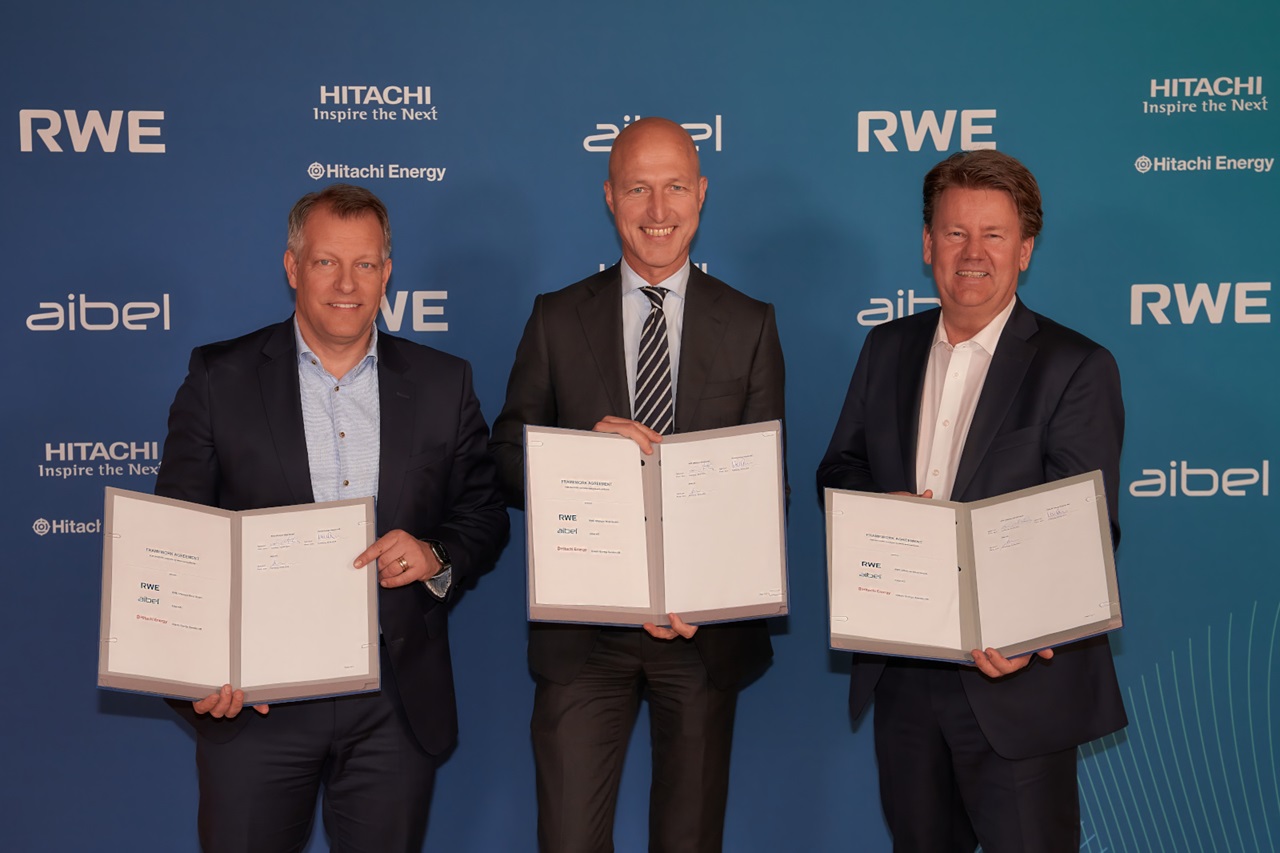 Three individuals hold open agreements against a blue branded backdrop featuring Hitachi, RWE, and Aibel logos.