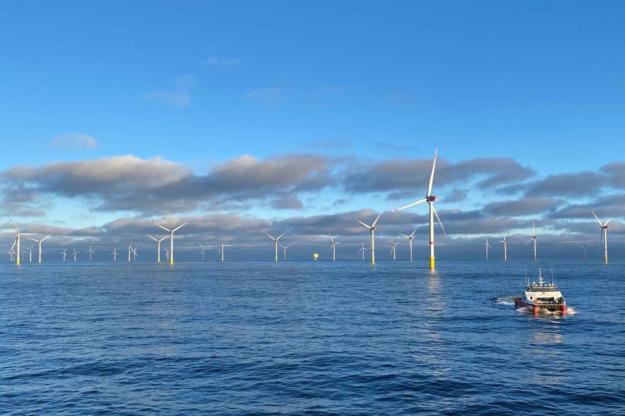 Ein Boot fährt durch ruhiges Wasser, umgeben von Windkraftanlagen mit einem klaren blauen Himmel und einigen Wolken.