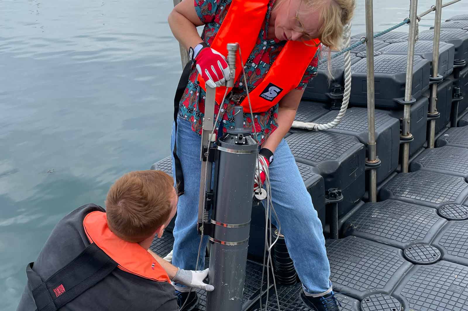 Zwei Personen arbeiten auf einem Forschungsschiff und bedienen wissenschaftliche Geräte in der Nähe des Wassers.