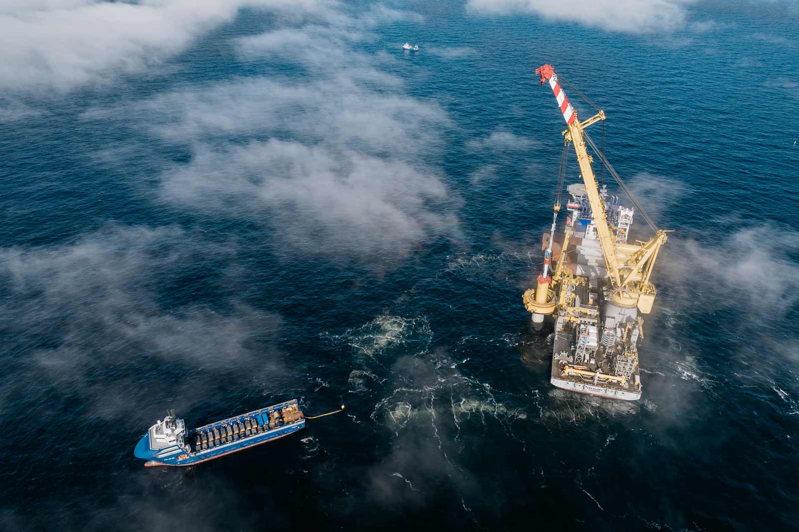 Die Installation eines Offshore Fundaments umgeben von Nebel, mit einem Schiff im Hafen und einem Kran, der arbeitet.