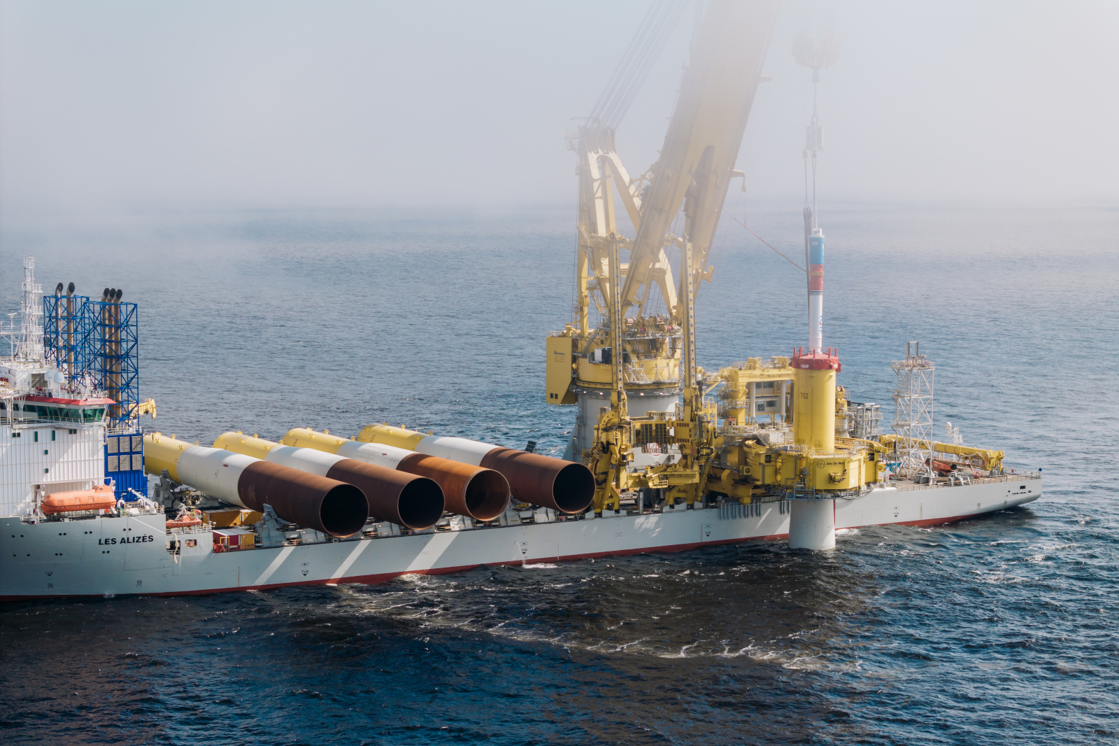 A large offshore construction vessel named Les Alizés, equipped for wind turbine installation, with multiple brown pipes.