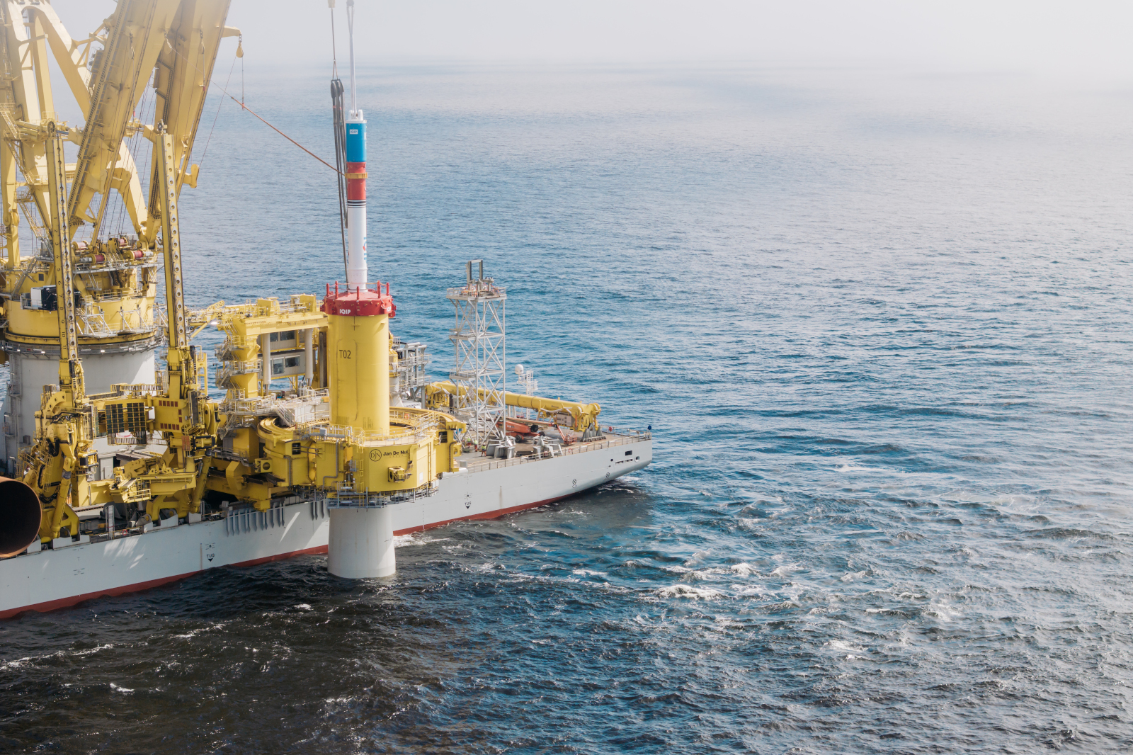 A large offshore vessel with yellow equipment is operating on the ocean surface, with a red structure visible in the centre.