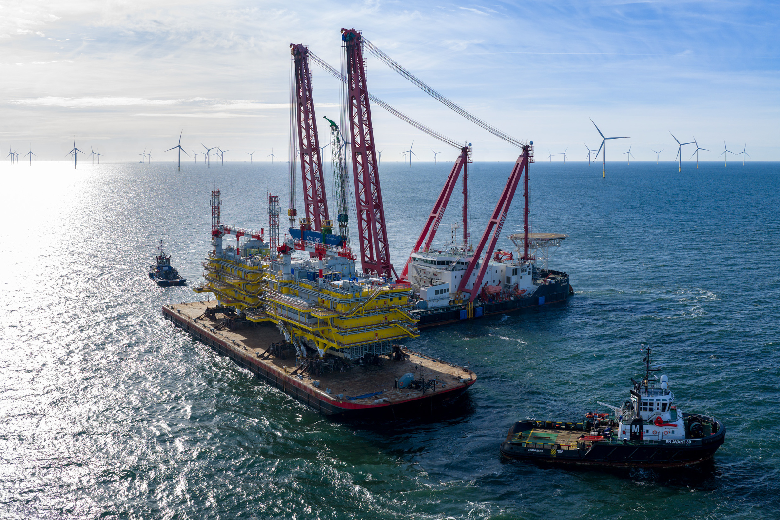 Schwerlastschiff transportiert gelbe Offshore Plattformmodule mit Schleppern.