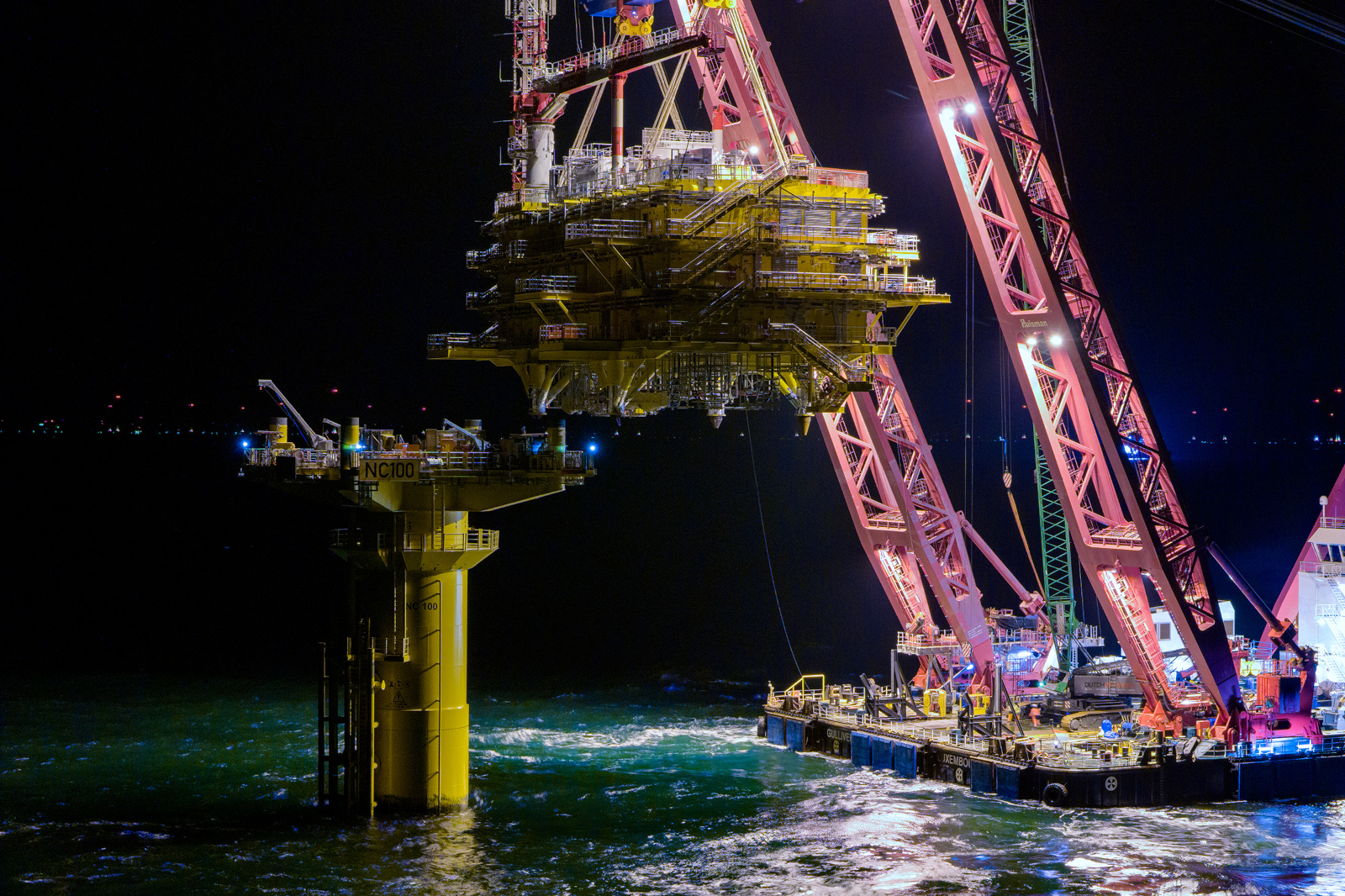 Beleuchtete Offshore-Plattform von rotem Schwimmkran bei Nacht.