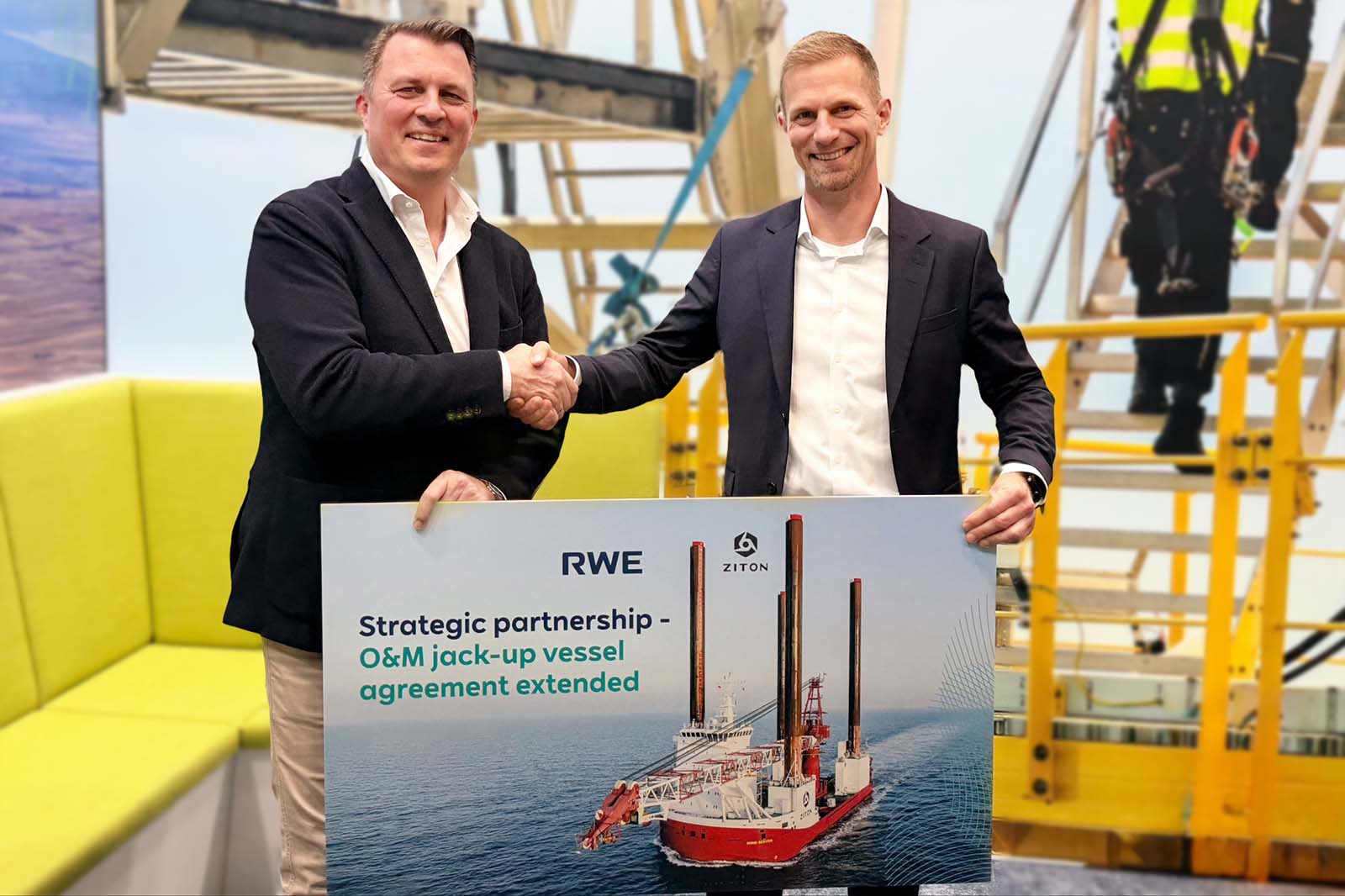 Two men in dark blazers hold a poster of a red-and-white jack-up vessel; the sign reads "RWE" and "Strategic partnership - O&M jack-up vessel agreement extended".