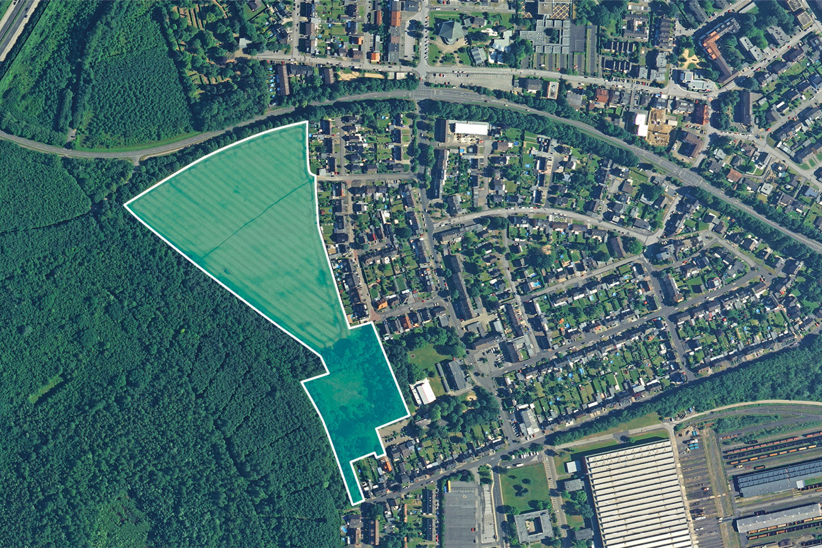 Eine Luftaufnahme eines grünen Feldes, umgeben von Häusern und Bäumen, die eine Mischung aus Wohn- und Naturlandschaften zeigt.
