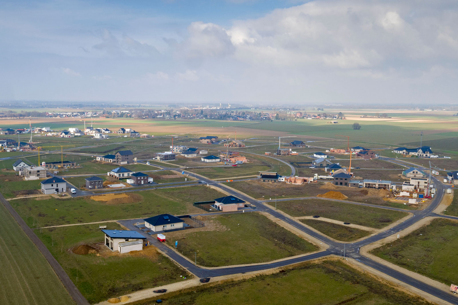 Luftaufnahme eines sich entwickelnden Wohngebiets mit verschiedenen im Bau befindlichen Häusern und grünen Feldern im Hintergrund.