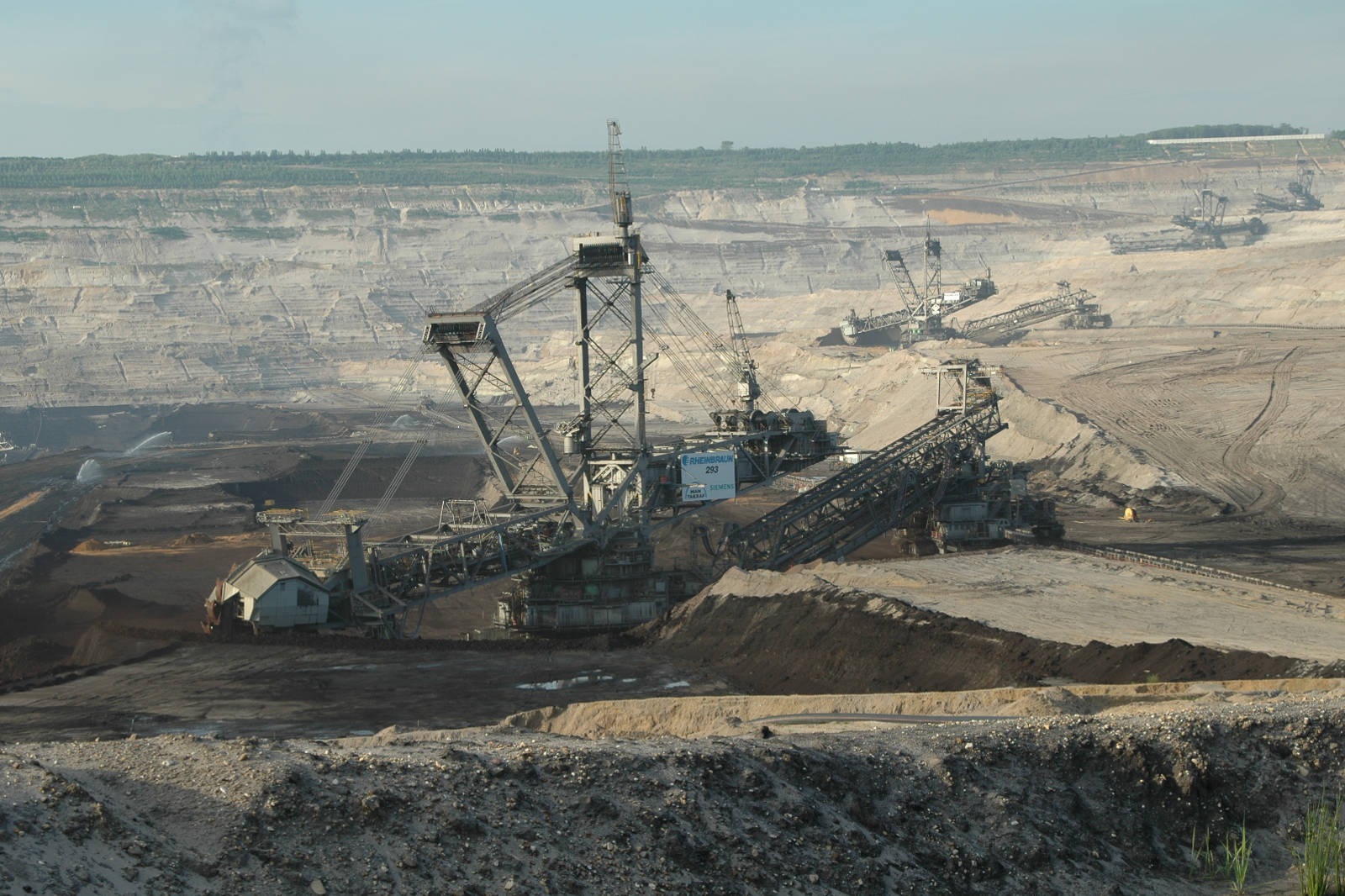 Eine große Tagebaumine mit Baggern und Förderbändern in einer weitläufigen Landschaft aus Erde und Gestein.