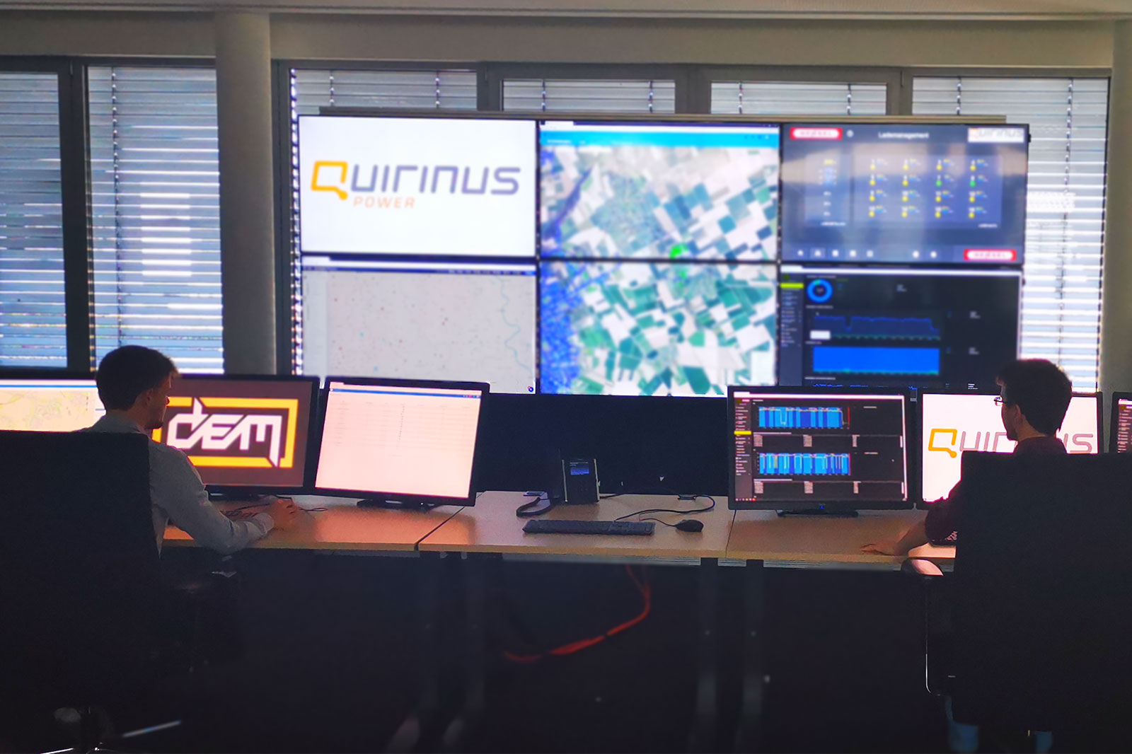 Zwei Fachleute überwachen Daten auf mehreren Bildschirmen in einem modernen Büro mit der Marke Quirinus Power.