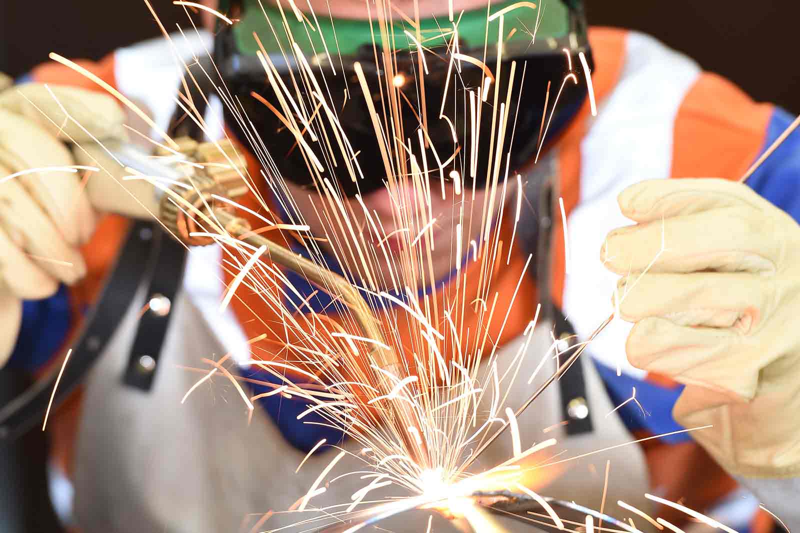 Ein Schweißer in Schutzausrüstung erzeugt Funken, während er an einer Metalloberfläche arbeitet.