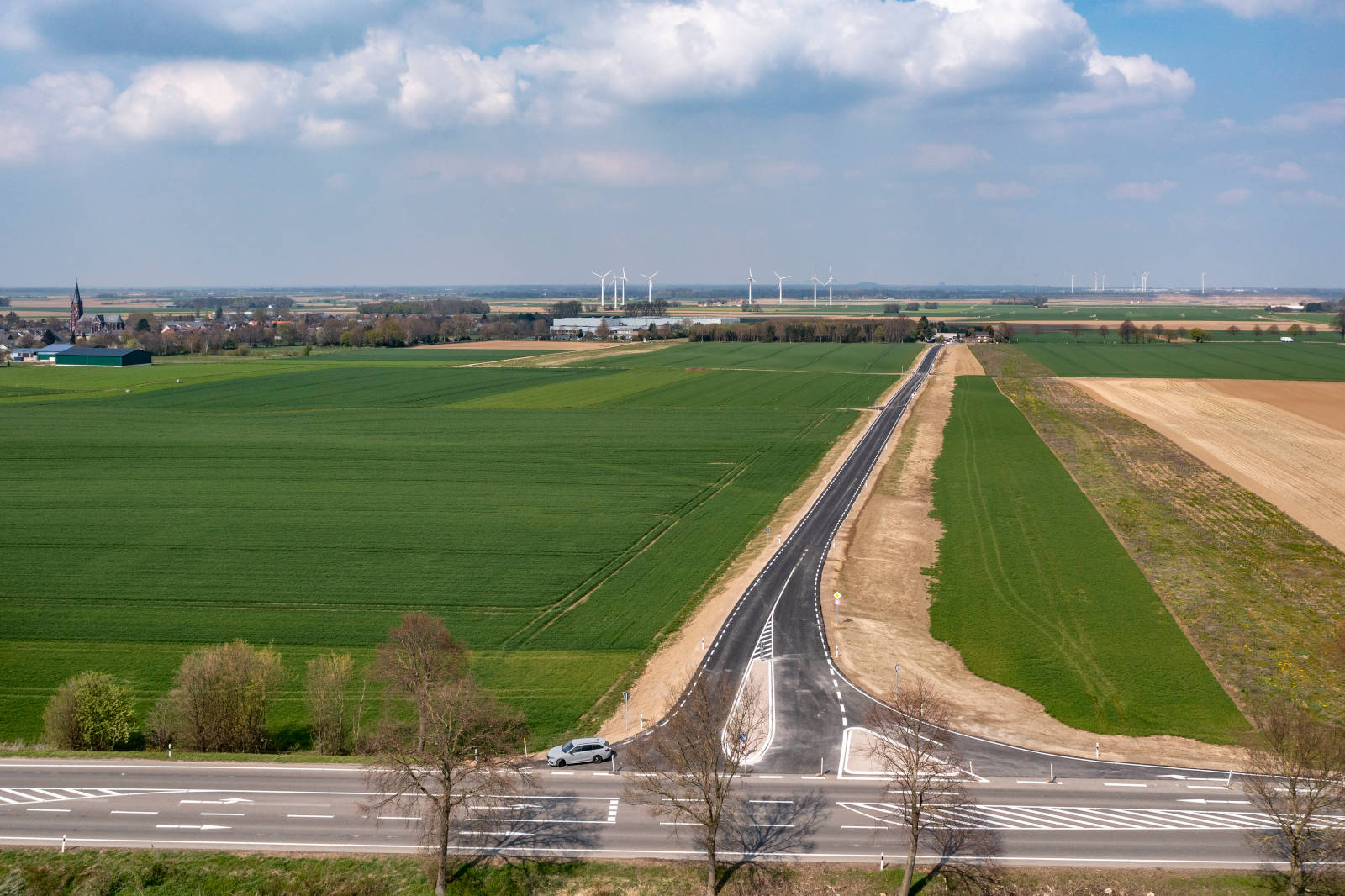 Eine malerische Aussicht auf eine ländliche Landschaft mit grünen Feldern, einer neuen Straße und Windturbinen in der Ferne.