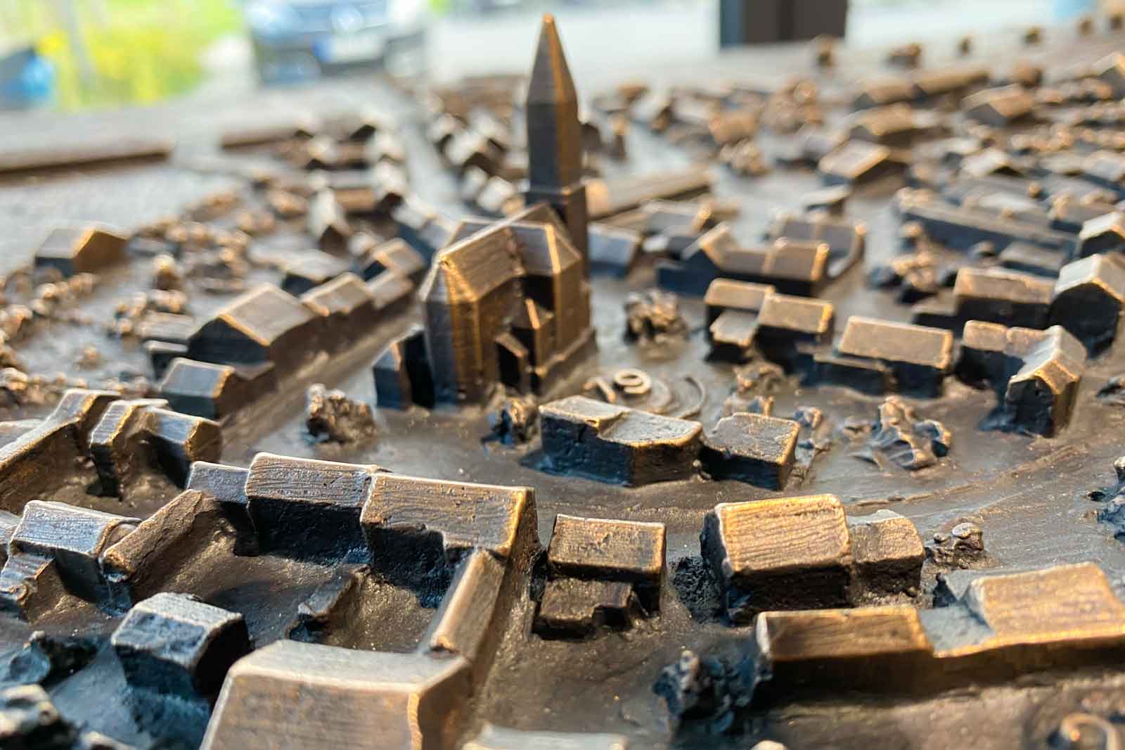 Ein detailliertes Modell, das ein Stadtlayout mit einem markanten Kirchturm in der Mitte und kleinen Gebäuden darstellt.