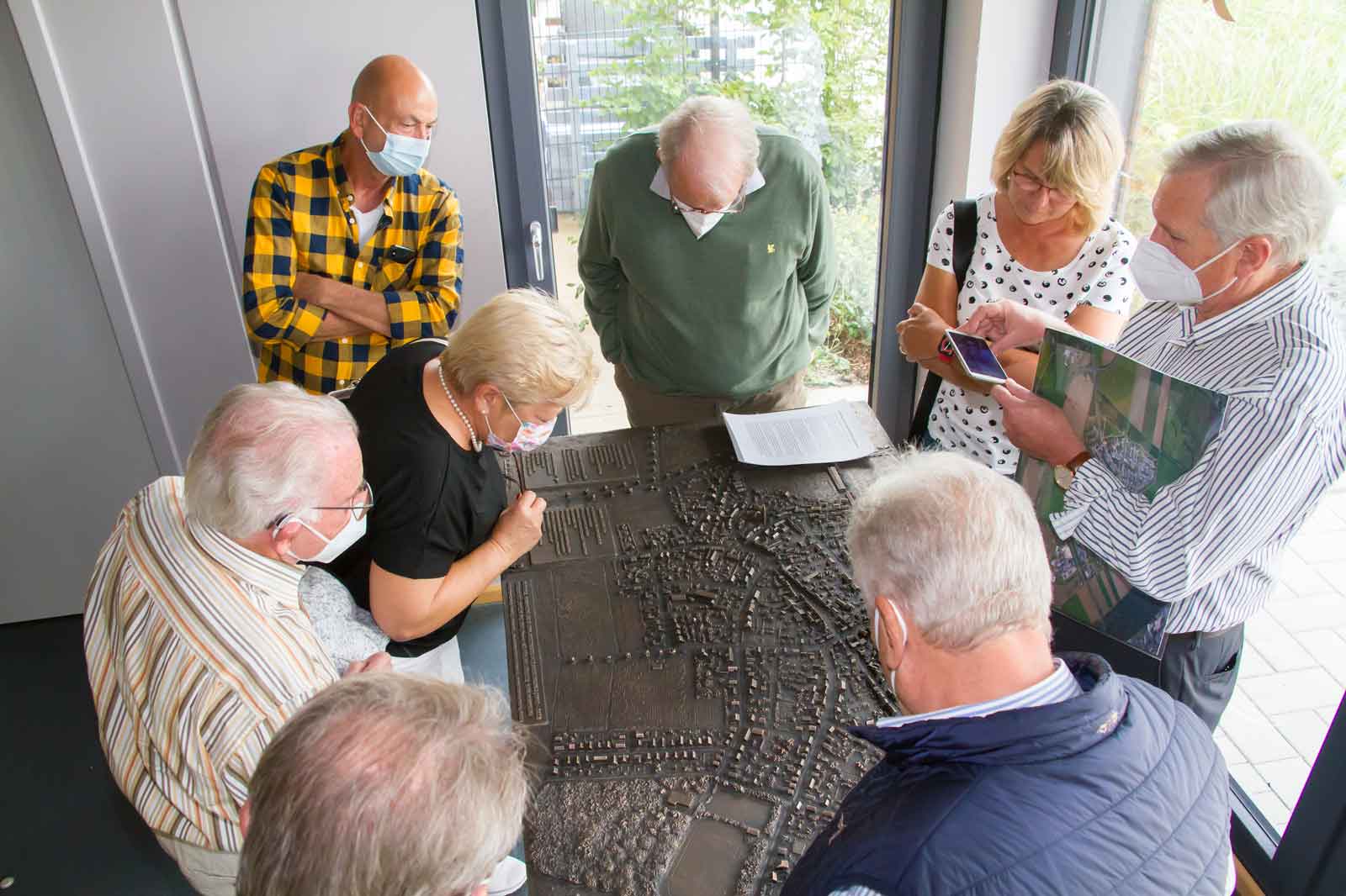 Eine Gruppe von Menschen betrachtet ein detailliertes Modell in einem hellen Raum, mit Grünanlagen draußen am Fenster.