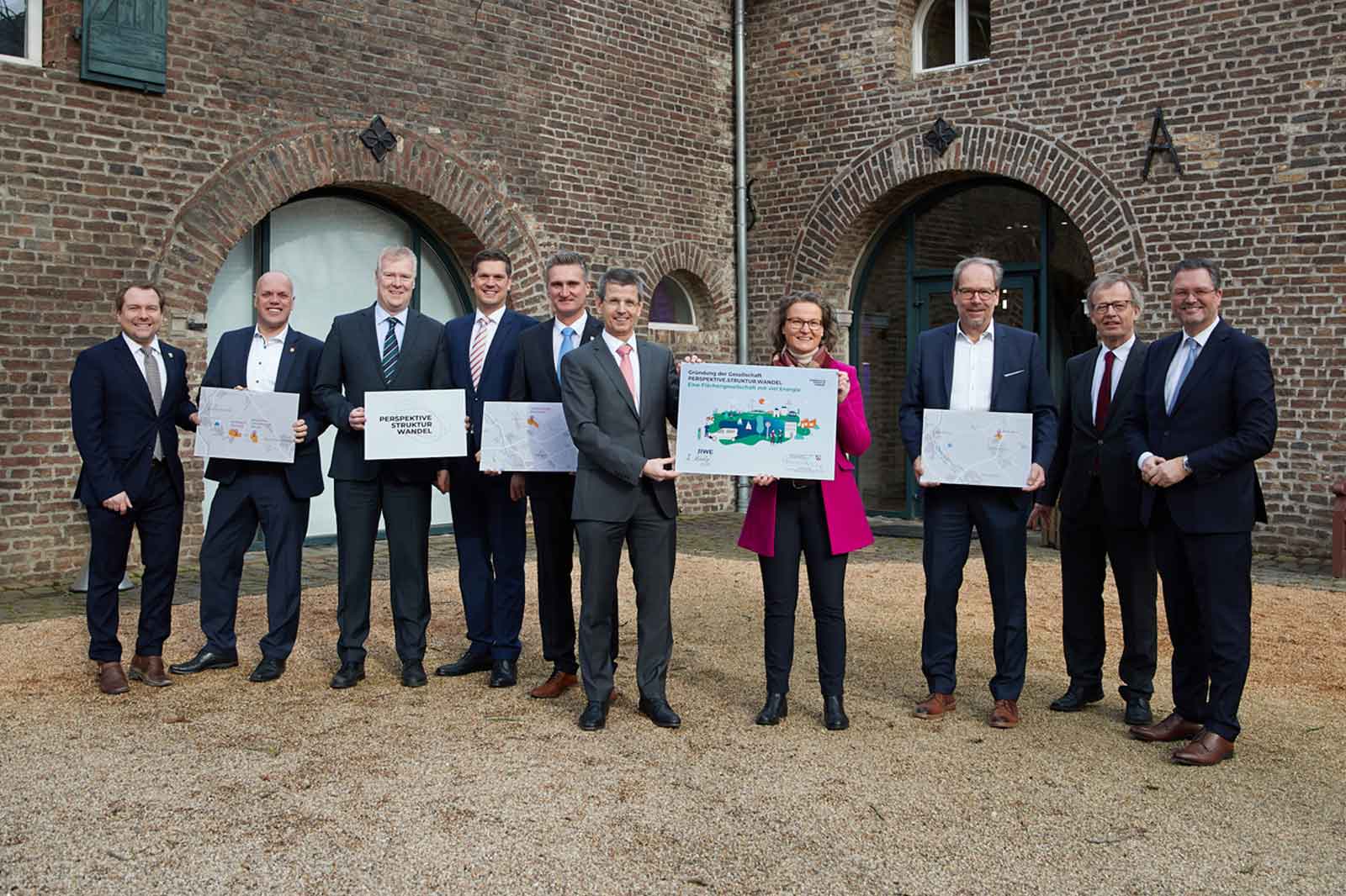 Eine Gruppe von Fachleuten hält Außenansichten in der Nähe eines historischen Ziegelgebäudes und diskutiert Entwicklungspläne.