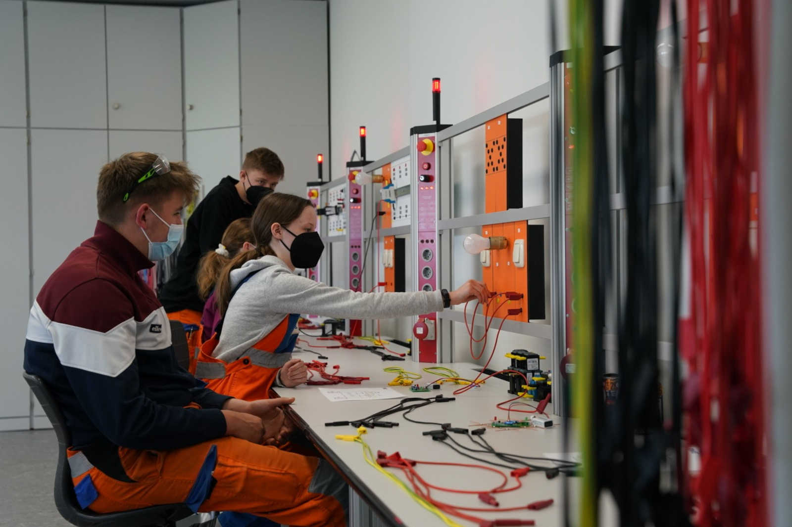 Schüler arbeiten in einer Ausbildungsstätte an elektrischen Schaltungen, verbinden Drähte und testen Geräte an Arbeitsplätzen.