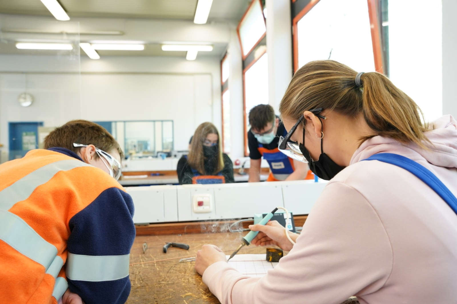 Schüler in einer praktischen Werkstatt, die sich auf Aufgaben mit Werkzeugen und Materialien in einem hellen Klassenraum konzentrieren.