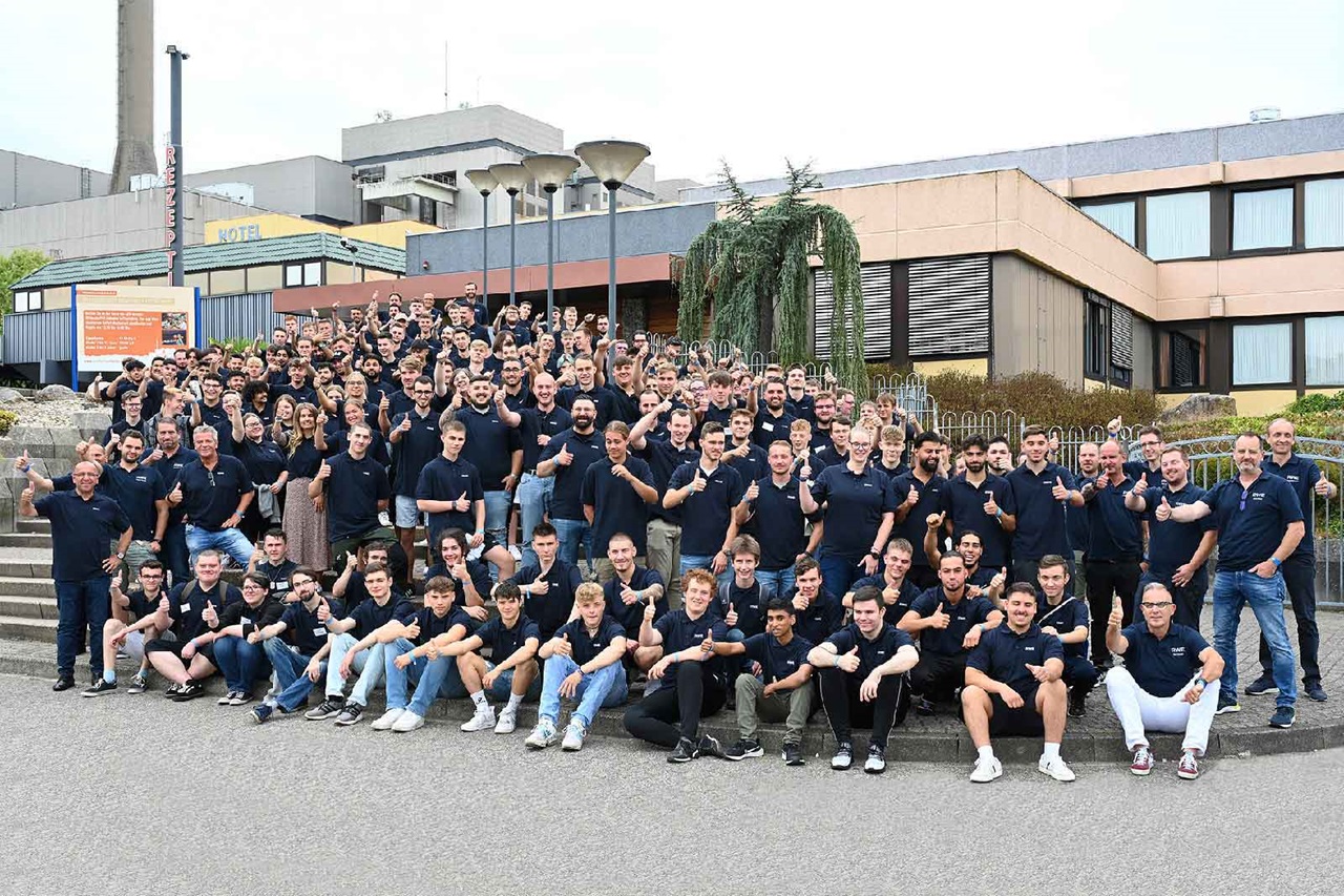Eine große Gruppe von Menschen in navyblauen T-Shirts, die draußen zusammen posieren und fröhlich aussehen.