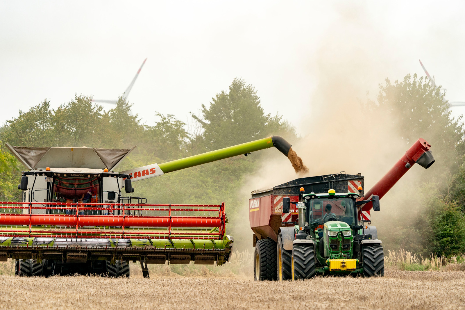 Ein Mähdrescher entleert Getreide in einen Anhänger, während ein Traktor neben ihm auf einem Feld steht.