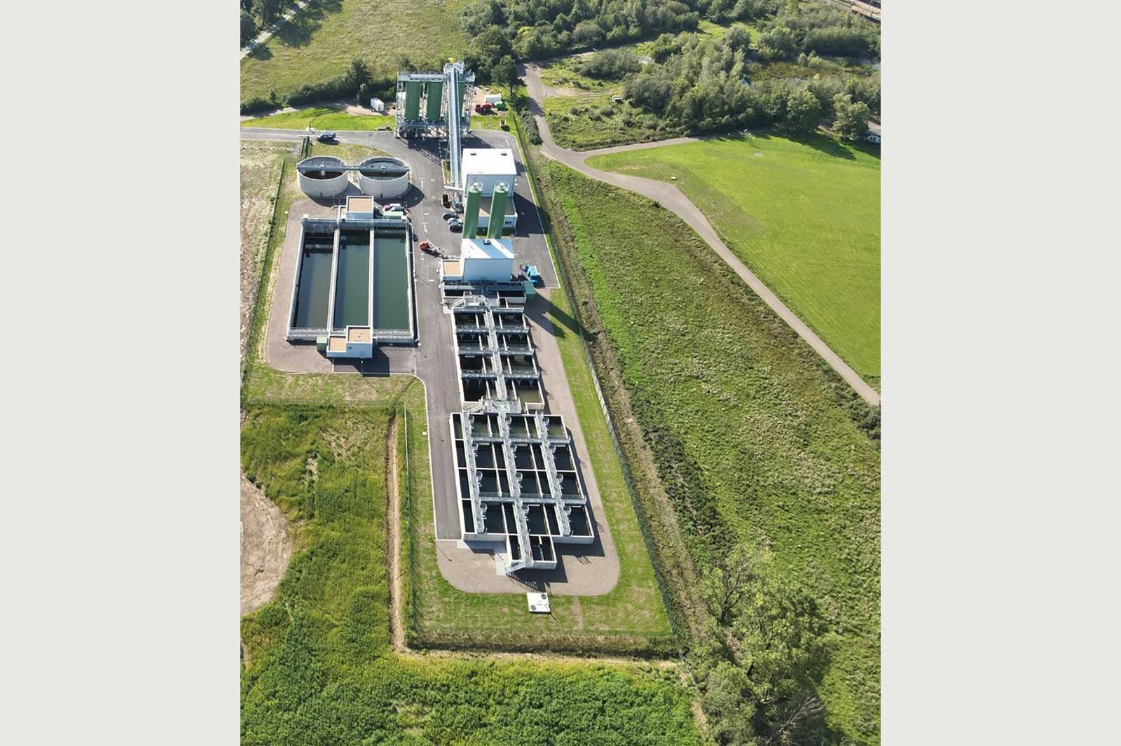 Luftansicht eines modernen Klärwerks mit runden und rechteckigen Becken, umgeben von Grünflächen.