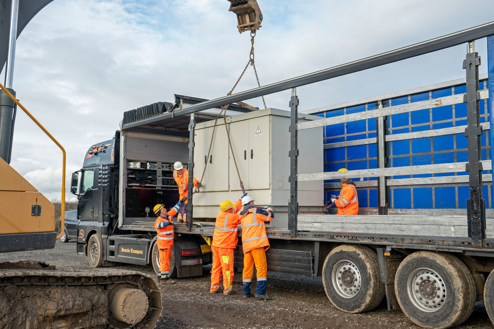 Arbeiter in Sicherheitskleidung entladen einen großen Container mit einem Kran von einem Lastwagen an einer Baustelle.