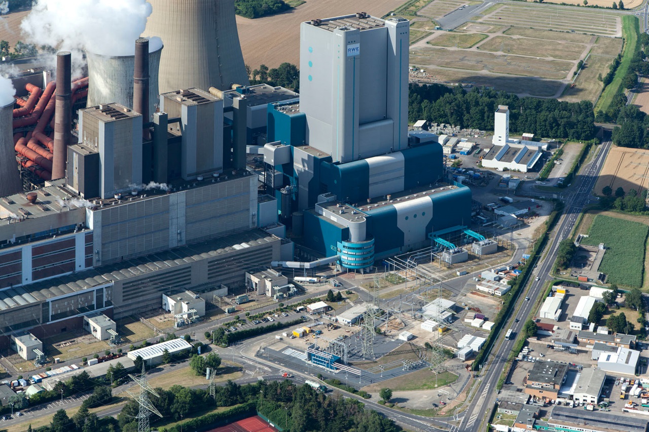 Eine Luftaufnahme eines Industrie-Kraftwerks mit Kühltürmen, Schornsteinen und umliegender Infrastruktur.