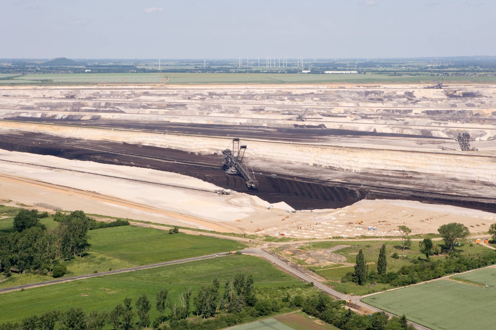 Luftaufnahme eines großen Tagebaus mit Maschinen und geschichteten Erden im Hintergrund von Feldern.