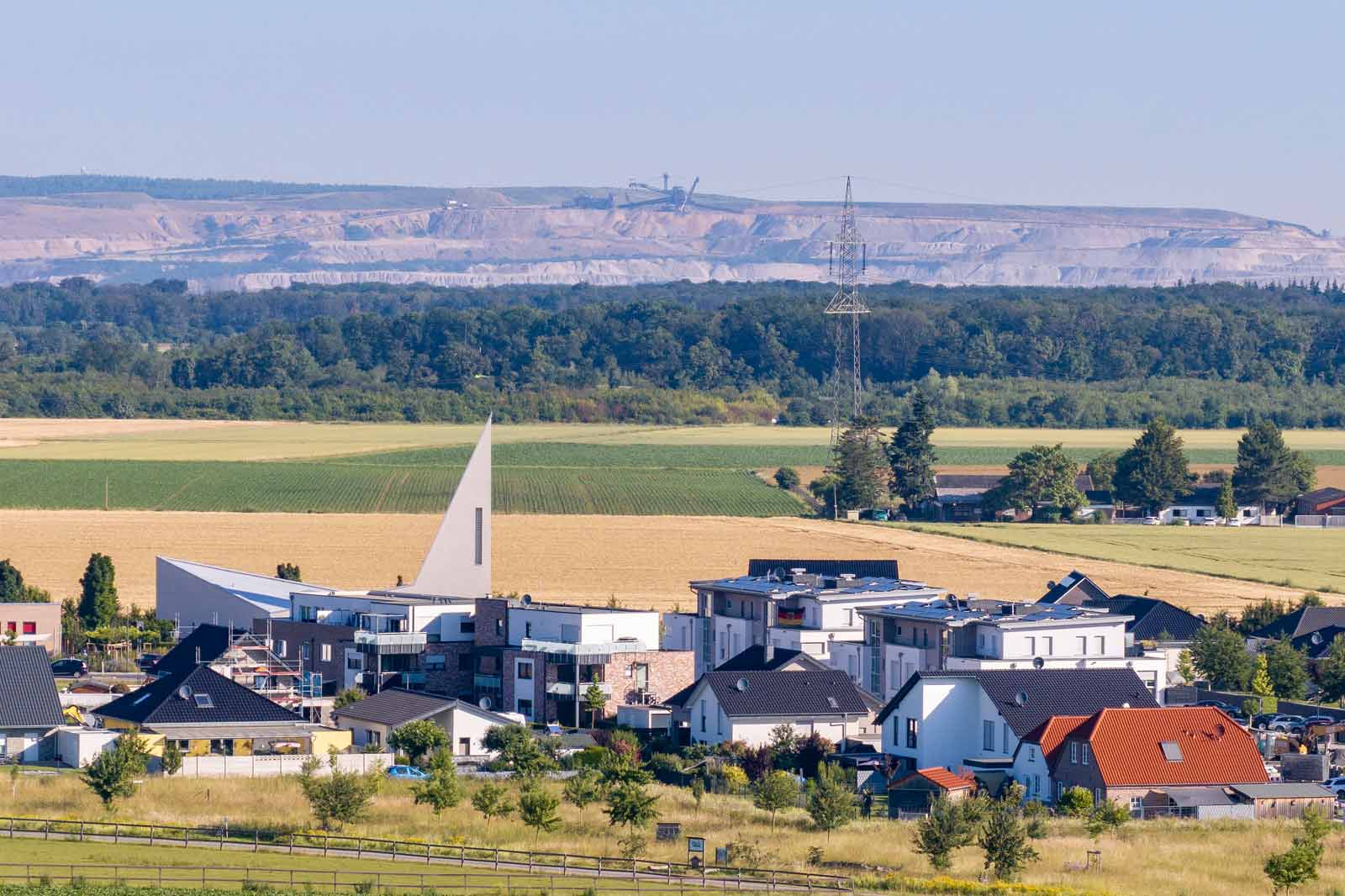 Eine malerische Aussicht auf moderne Häuser in einer ländlichen Gegend mit Feldern und entfernten Hügeln im Hintergrund.