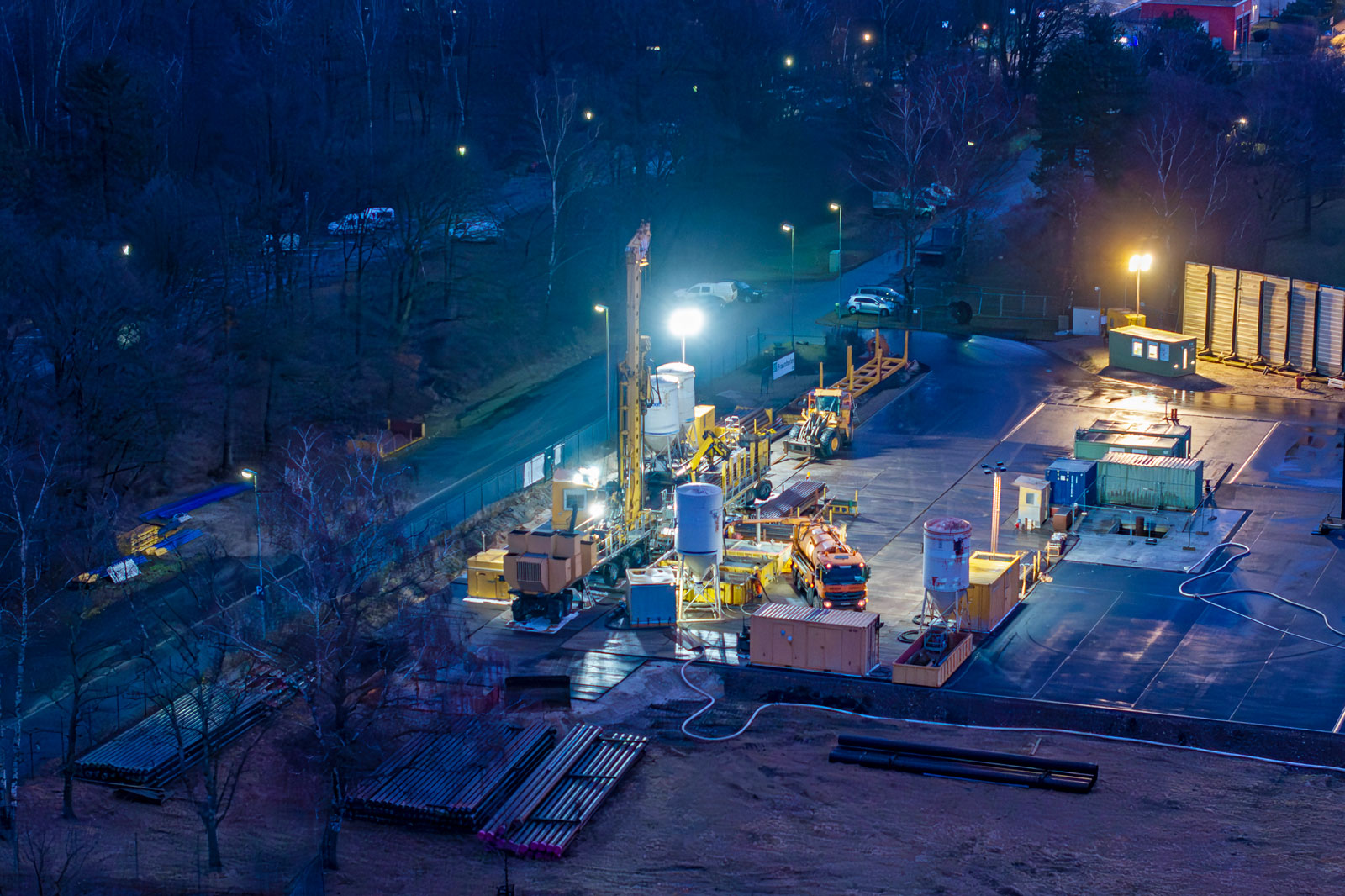 Eine nächtliche Ansicht einer aktiven Bohrstelle, beleuchtet von hellen Lichtern und mit Maschinen sowie Lagerräumen.