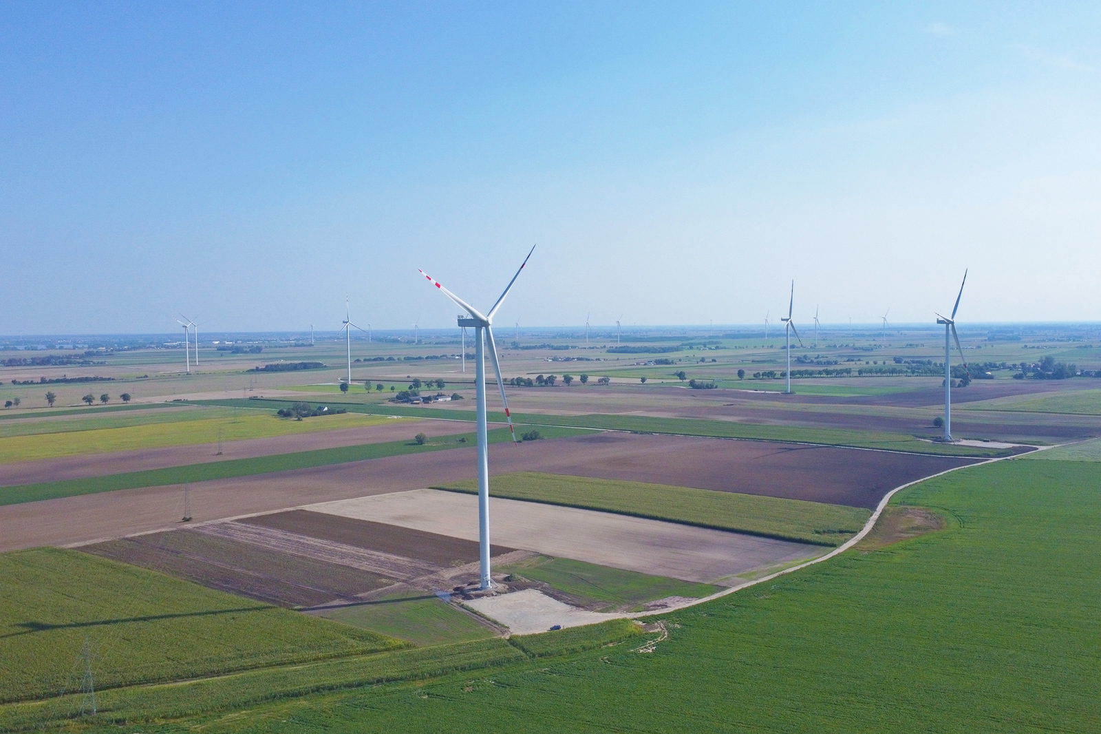 Eine weitläufige Landschaft mit Windkraftanlagen, die auf grünen Feldern und Ackerland stehen.