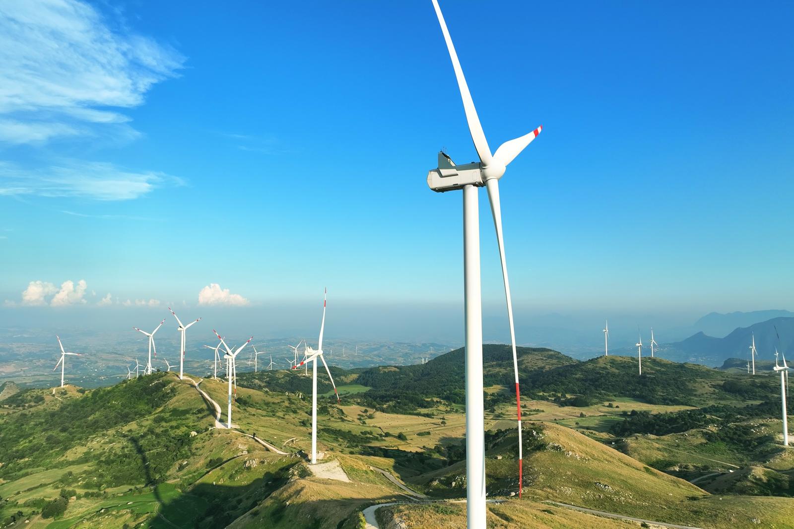 A landscape with multiple wind turbines on green hills under a clear blue sky, showcasing renewable energy in nature.