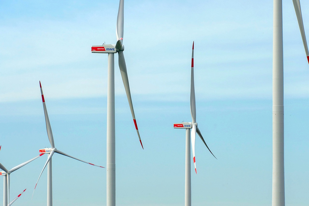 Eine Gruppe von Windkraftanlagen vor einem klaren Himmel, mit roten und weißen Akzenten auf den Rotorblättern und Turmstrukturen.