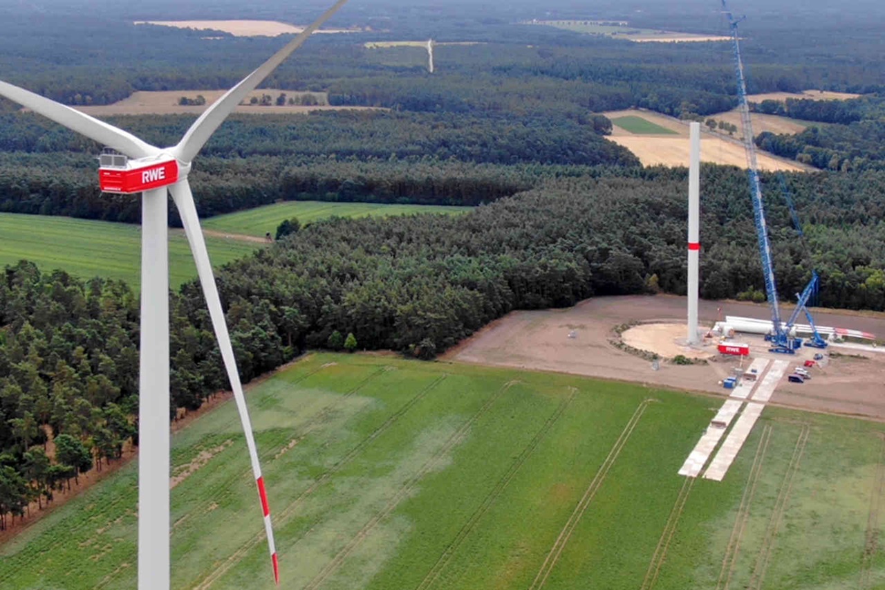 Ein Windkraftwerk mit RWE-Branding, vor einer grünen Landschaft und einer Baustelle im Hintergrund.