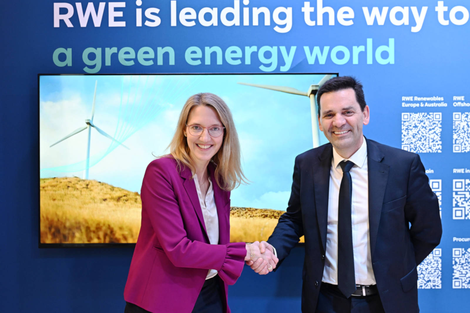 Zwei Personen schütteln sich die Hände vor einem blauen Hintergrund, der RWE's Engagement für grüne Energie mit einem Windrad zeigt.
