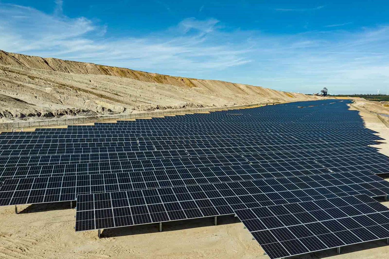 Ein großer Solarpark auf einer sandigen Landschaft unter einem klaren blauen Himmel.
