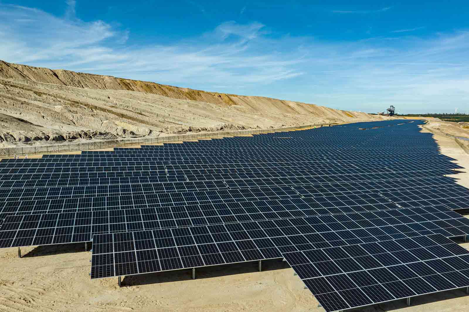 Ein großer Solarpark auf einer sandigen Landschaft unter einem klaren blauen Himmel.