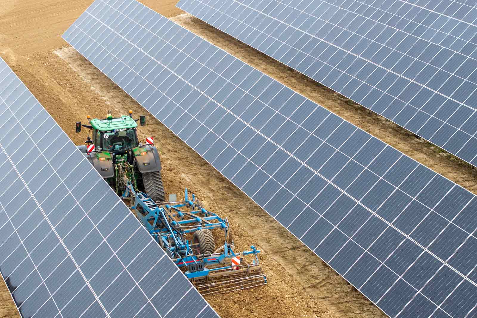 Ein Traktor pflügt zwischen Reihen von Solarpanelen auf einem Feld, was nachhaltige Landwirtschaftspraktiken zeigt.