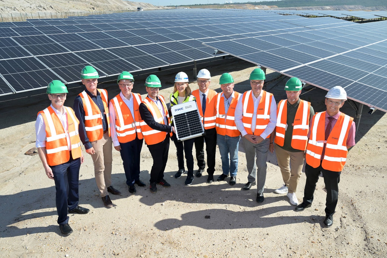 Eine Gruppe von Personen in Sicherheitswesten und Helmen steht in der Nähe von Solarpanelen und hält ein Solarpanel.