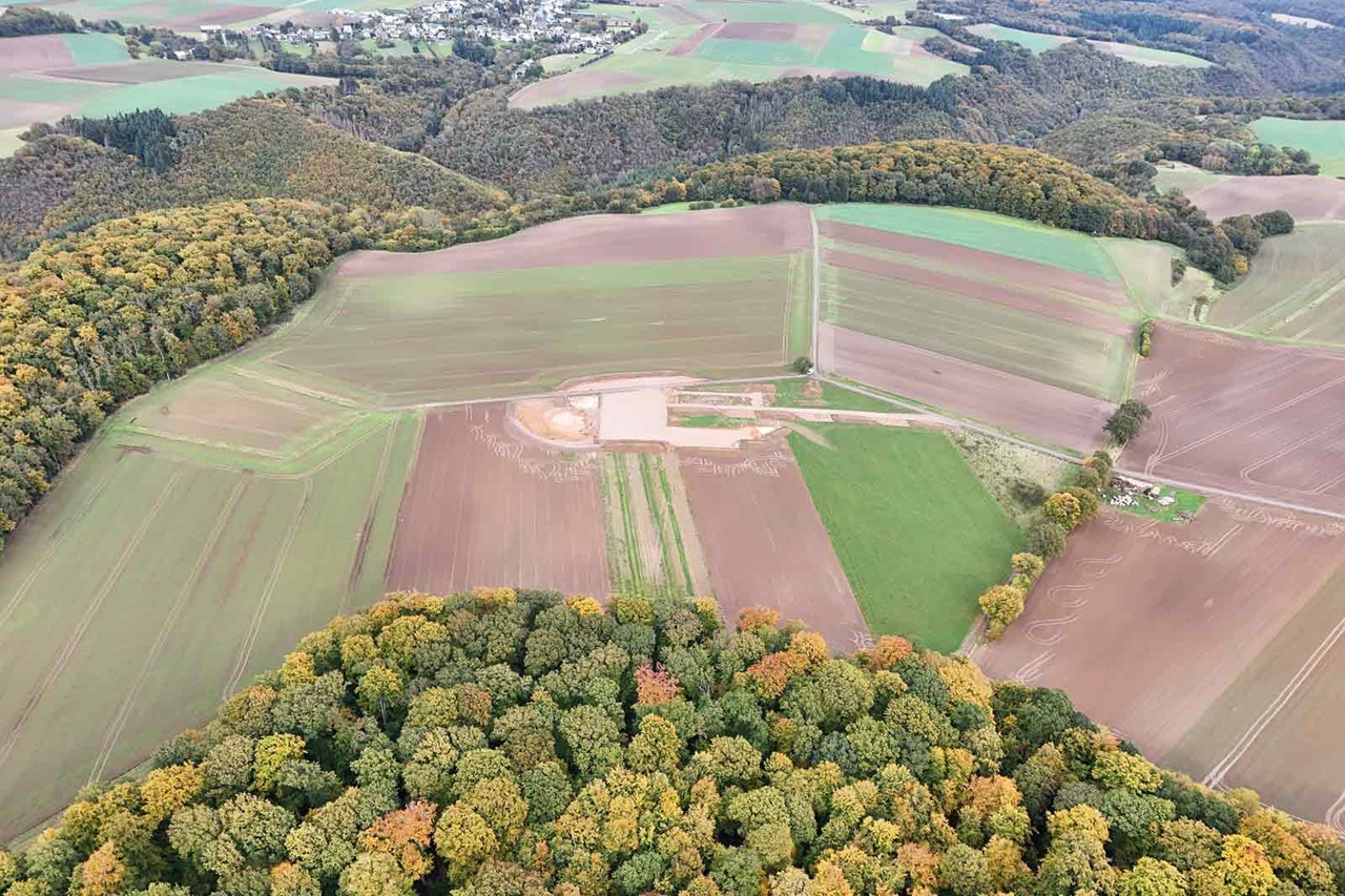 Eine Luftaufnahme von landwirtschaftlichen Flächen, Feldern und bewaldeten Gebieten mit einer kleinen Baustelle.