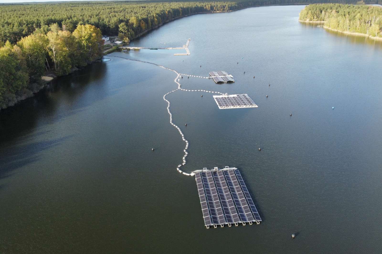 Aerial view of solar panels on a lake, surrounded by a forest and calm water.