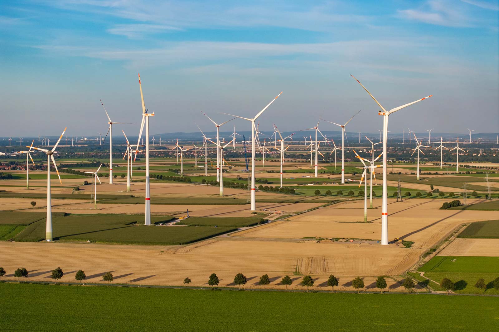 Luftaufnahme einer weiten Landschaft, die mit Windkraftanlagen unter einem klaren blauen Himmel übersät ist.