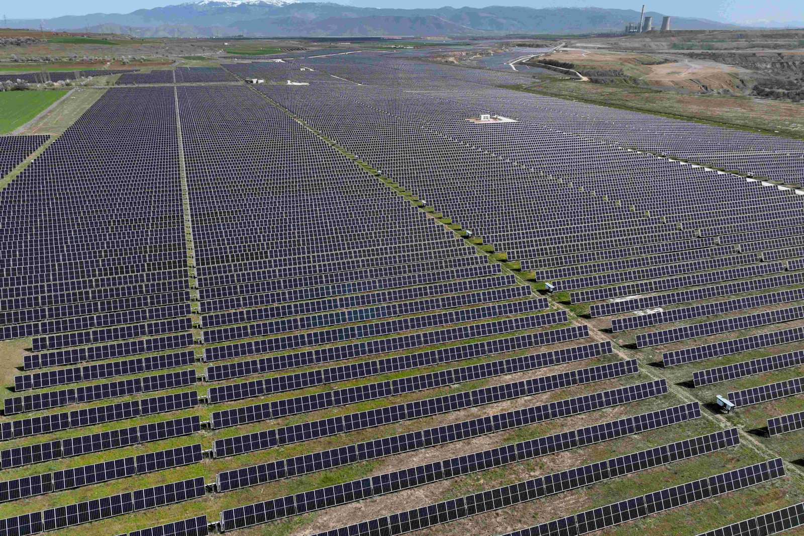 A vast solar farm with numerous solar panels arranged in rows under a clear sky, with mountains visible in the background.